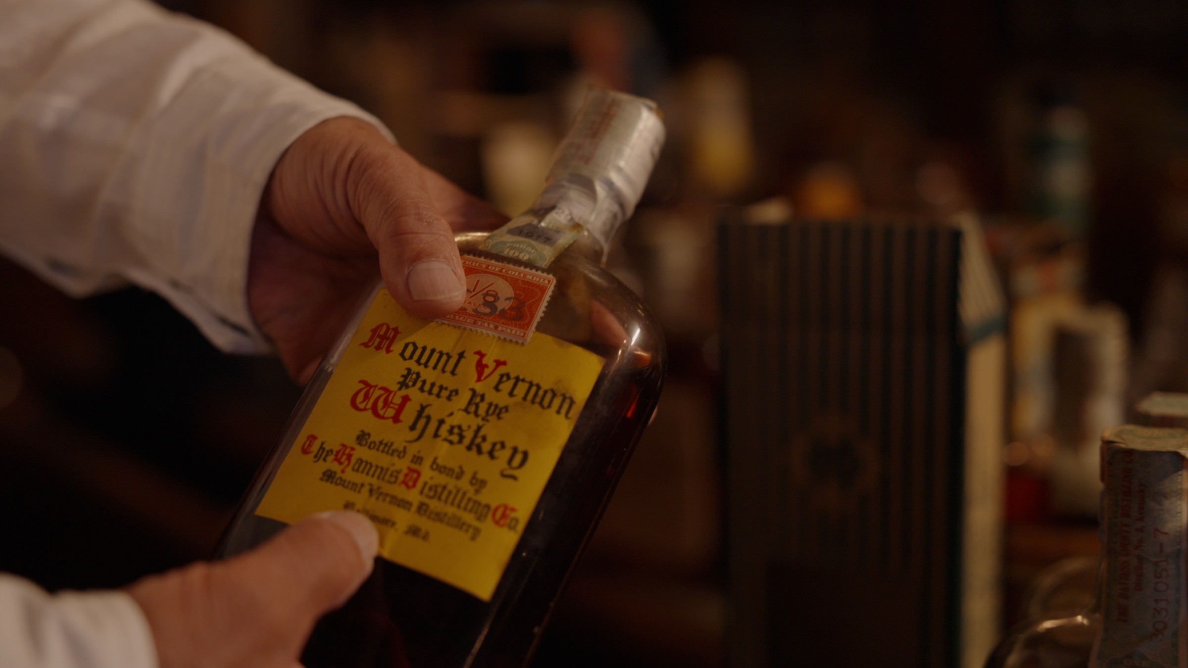 Hands holding an old bottle of Mount Vernon Pure Rye Whiskey, bottled in bond in Baltimore, in the low light of the bar