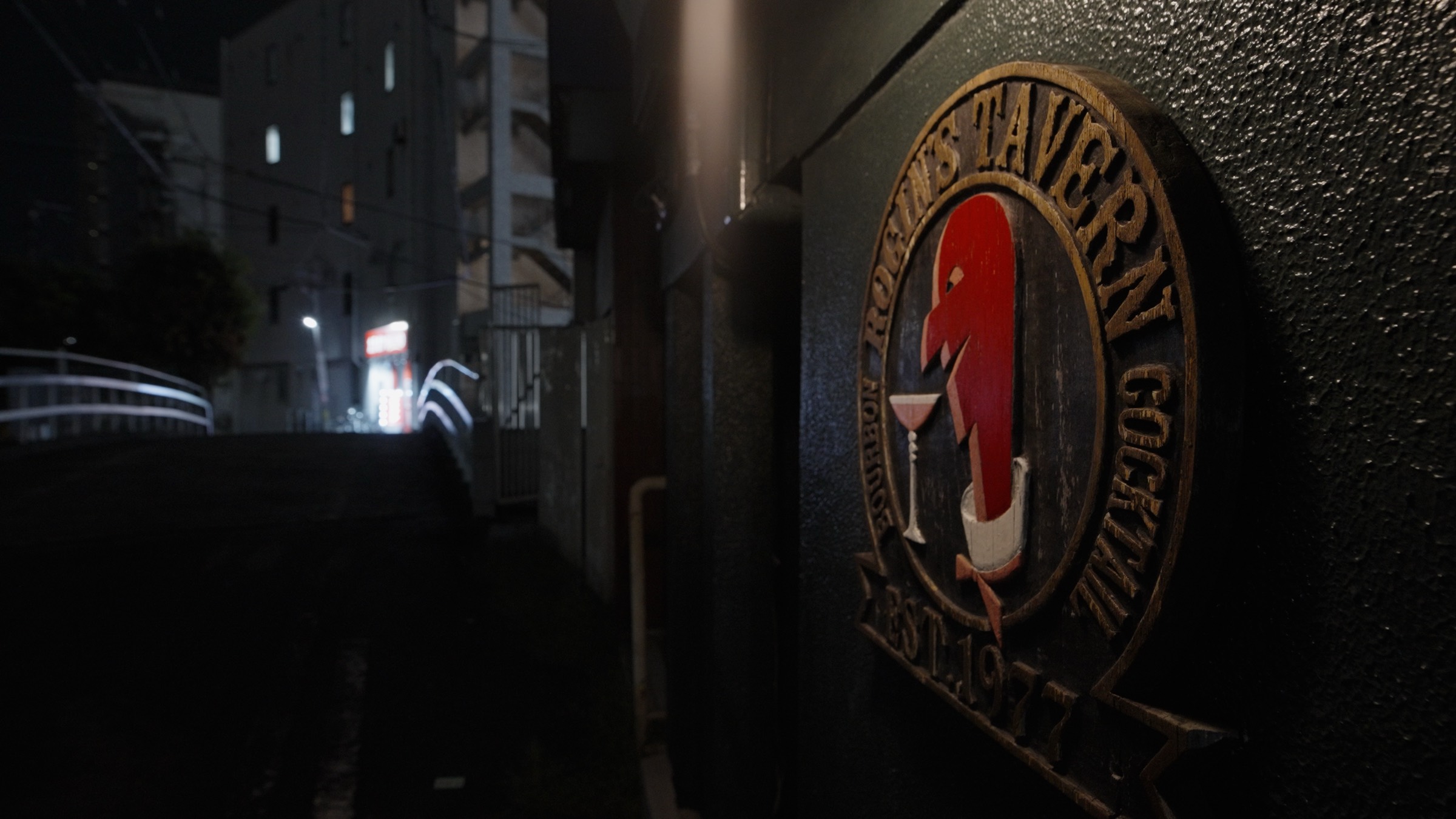 The Rogin's Tavern emblem, est. 1977, on a dark wall beside a narrow Moriguchi street at night